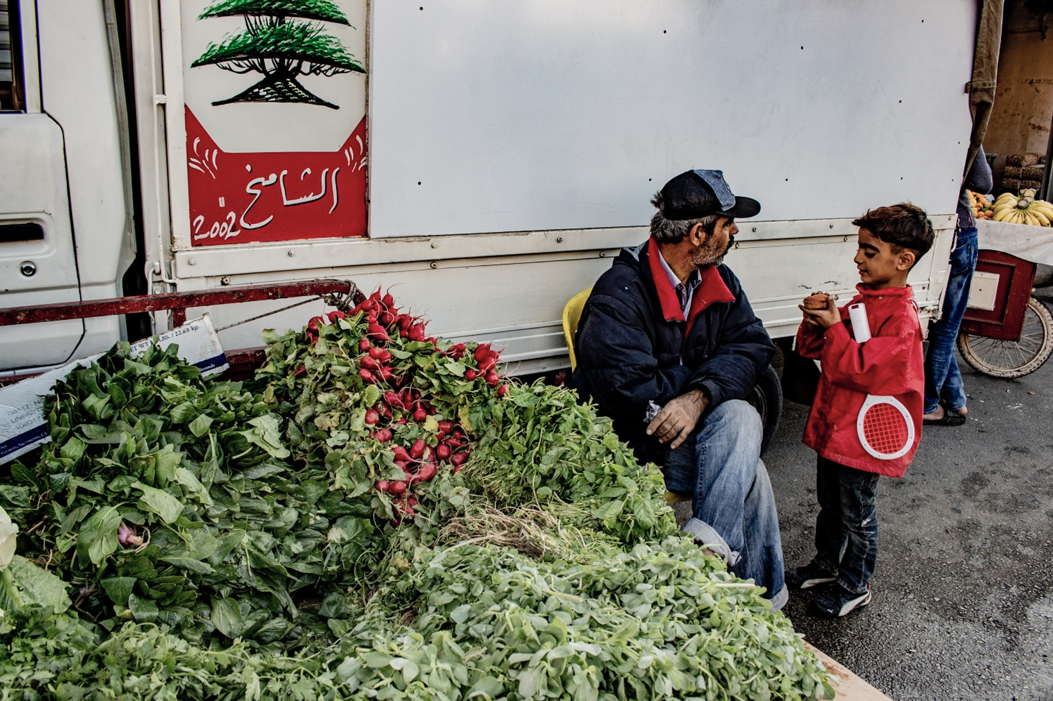 Caption: Young child chatting with his father, a greengrocer selling his fresh products in one of the streets of Beirut.  Photo credit: © RCO/Nadine Daou 